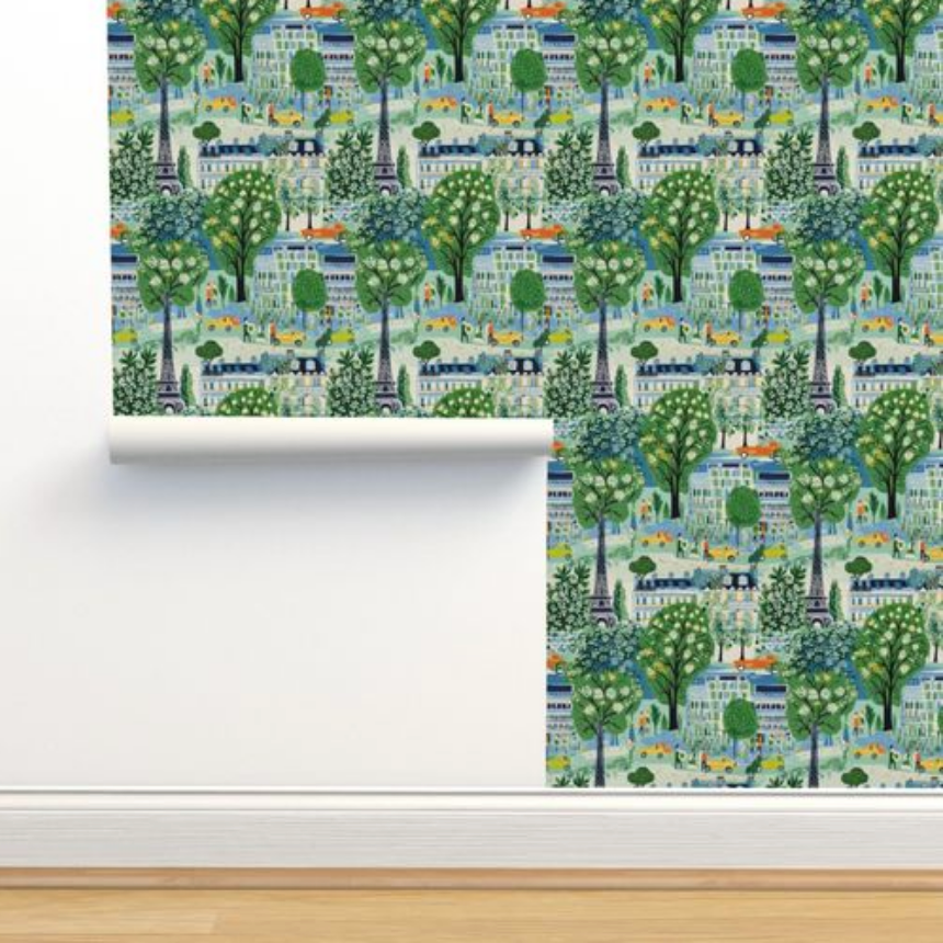 A roll of Spring in Paris Wallpaper from Stannie & Lloyd, with a colorful forest and town pattern, serving as unique wall decor, is partially unrolled against a wall.