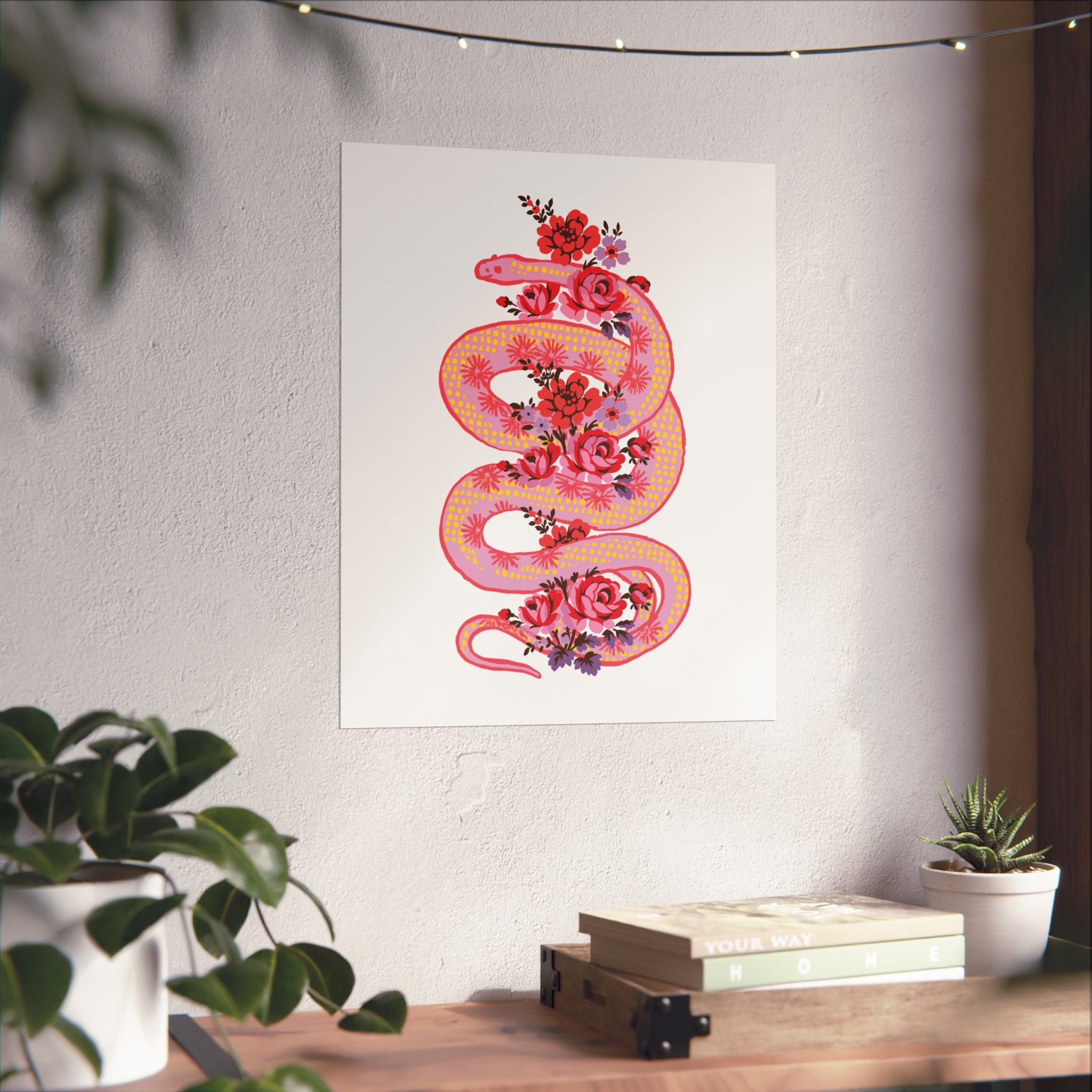 The "Snake with Roses" Large Matte Poster by Printify features a pink and orange snake with flowers, printed on museum-grade paper, displayed above a wooden desk with plants and books. Available in 7 sizes.