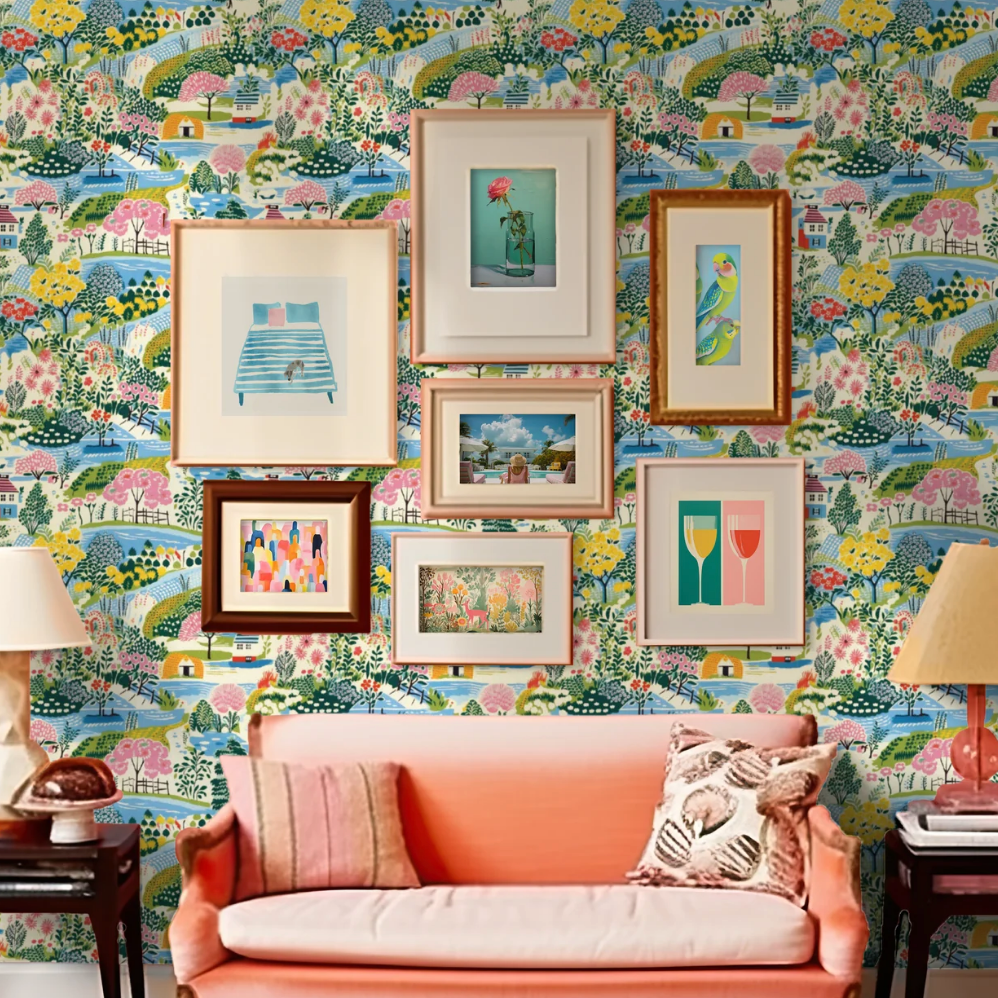 A living room with framed art and colorful wallpaper behind a coral couch.