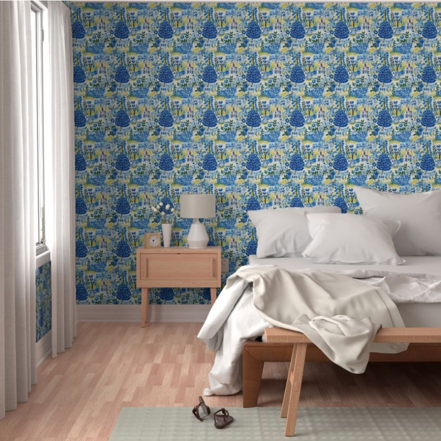 A bedroom featuring a bed with white bedding, a wooden nightstand with a lamp, art on walls, and Cozy Cottage in Blue Wallpaper by Stannie & Lloyd.