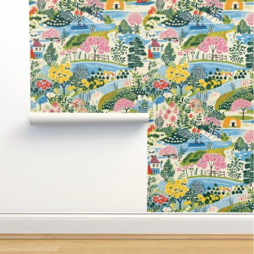 A roll of Colorful Cozy Village Wallpaper by Stannie & Lloyd is partially unrolled against a wall above a wooden floor, transforming it into wall art for the living room.