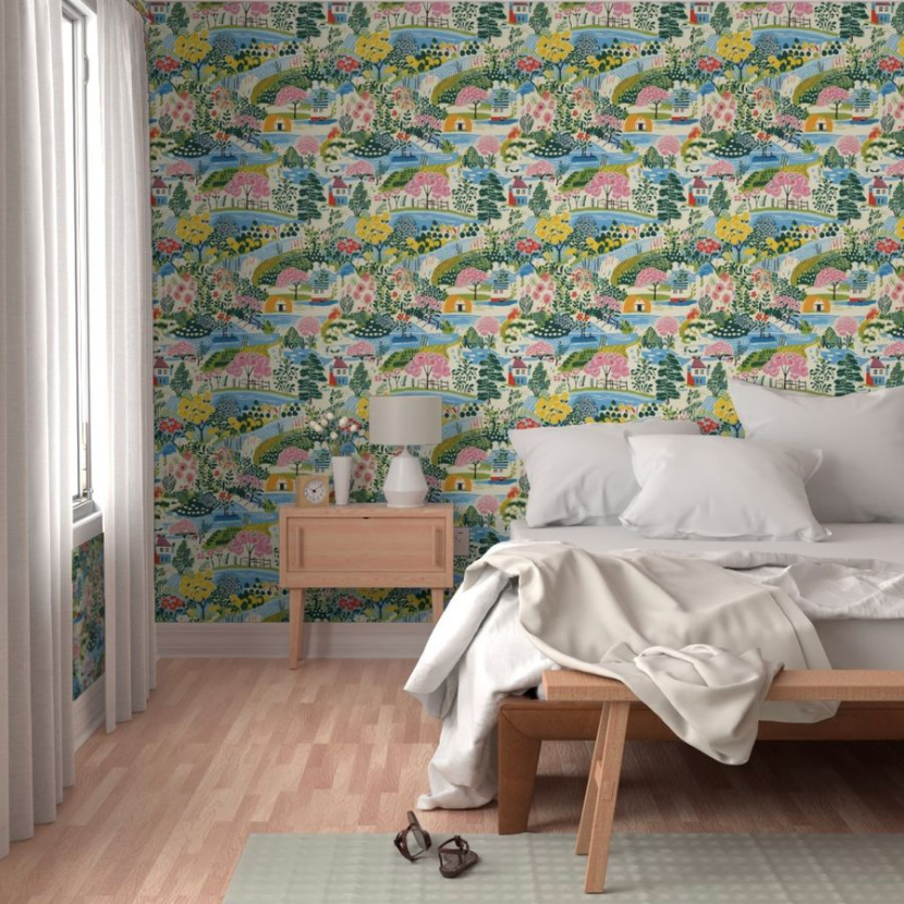 Brightly patterned Colorful Cozy Village Wallpaper from Stannie & Lloyd adorns the walls with art in a bedroom, featuring a simple bed, bedside table, and modern lamp.