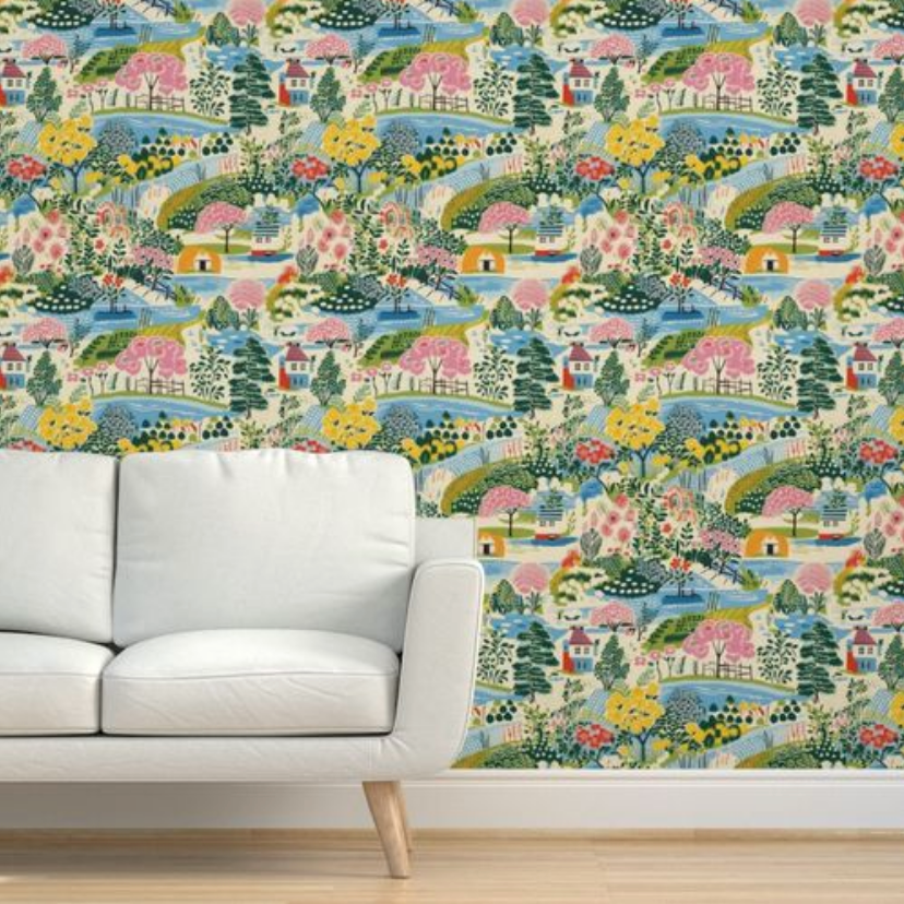 A white sofa against a wall with vibrant, Stannie & Lloyd Colorful Cozy Village Wallpaper featuring art prints of a floral and landscape design.