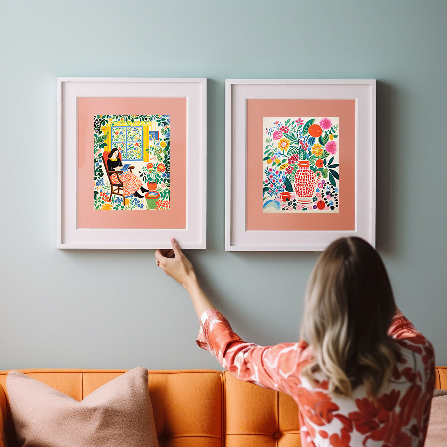 A woman is pointing to two framed art prints on an orange couch.